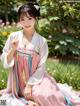 A woman in a pink and white hanbok sitting in the grass.