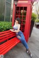 A woman sitting on a red bench in front of a red phone booth.