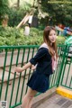 A woman in a school uniform leaning against a green fence.