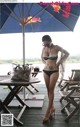 A woman in a bikini standing under an umbrella.