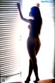 A nude woman standing in front of a window.