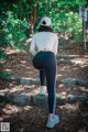 A woman in a white top and black leggings standing on a rock in the woods.