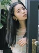 A woman with long black hair leaning against a gate.